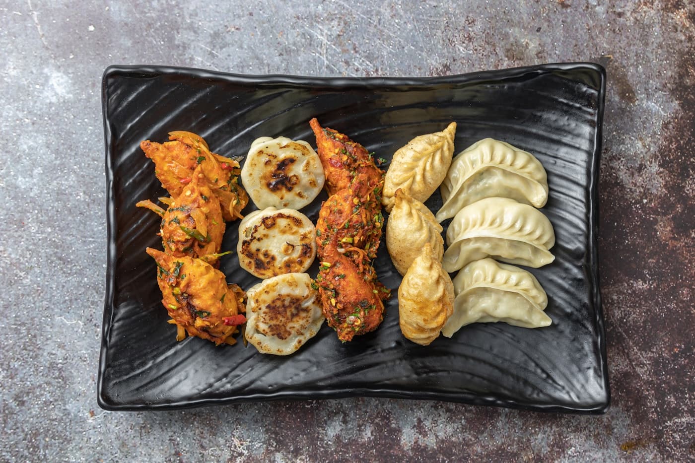 Colourful platter of steamed, fried, and chilli momos